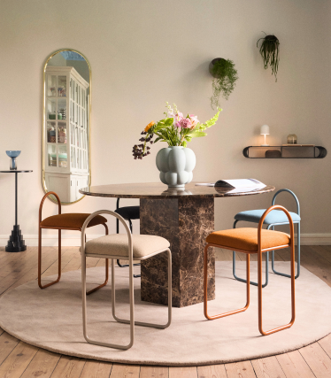 Elegant dining area with round marble table top, colourful chairs and sculptural vase, stylishly staged in a warm, harmonious ambience.