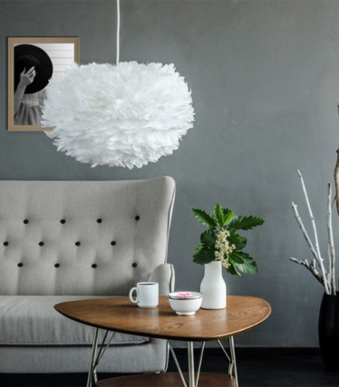 A white UMAGE pendant light made of feathers hangs above a stylish living area with a Scandinavian feel.