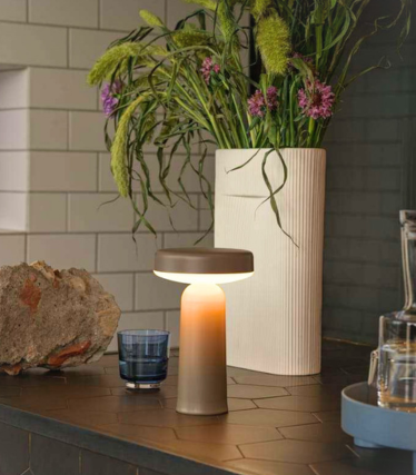 Portable Muuto table lamp on a dark kitchen worktop with floral decoration.