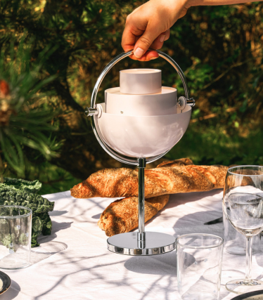 Portable GUBI table lamp on a stylishly set garden table in sunlight.