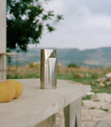 Brushed metal cup on an outdoor stone slab, with a soft landscape in the background.
