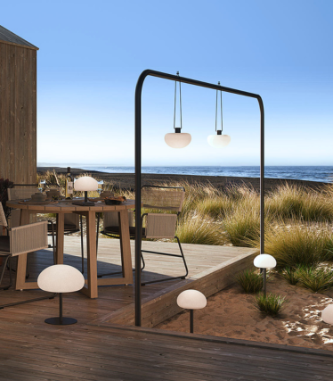 Outdoor lights on a wooden seaside terrace, casting a soft glow among dune grass.