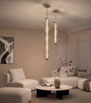 Two slender glass pendant lights above a marble coffee table in a bright living room with a white sofa and armchair.