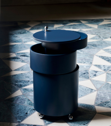 Dark blue cylindrical bar cart by Verpan with wheels and removable lid on a patterned stone floor.